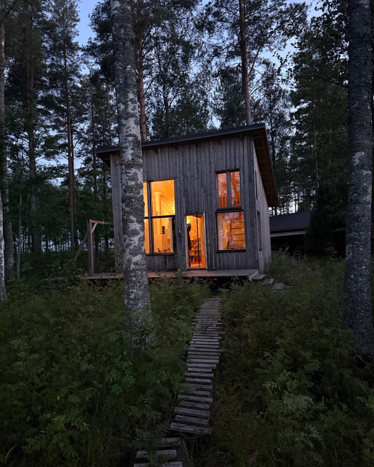The Utopia & Utility studio in Finland, a timber cabin glowing at dusk among birch and pine trees